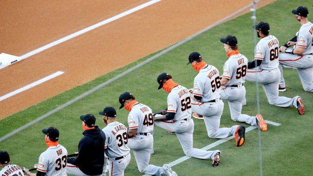 The San Francisco Giants kneel and hold a black ribbon to show their support for social justice and diversity and inclusion in baseball during the pre-game ceremony prior to the game between the Giants and the Los Angeles Dodgers at Dodger Stadium on July 23, 2020. Photo: Rob Leiter/MLB Photos via Getty Images