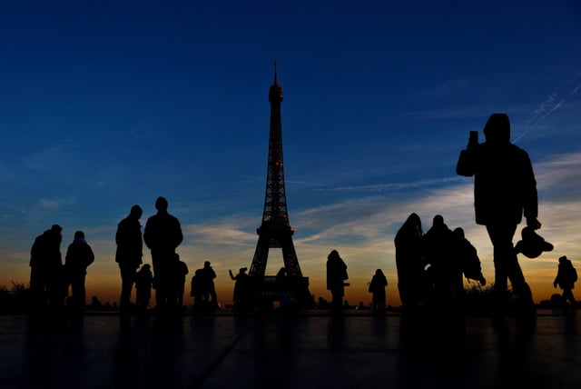 Tourists are silhouetted against the sunset as they take pictures on a cold day in Trocadero Square near the Eiffel Tower in Paris, France, January 14, 2025. REUTERS/Gonzalo Fuentes/File Photo