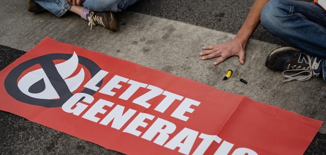 Ein Mitglied der „Letzten Generation“, der seine Hand selbst auf der Straße festgeklebt hat, blockiert eine Kreuzung
