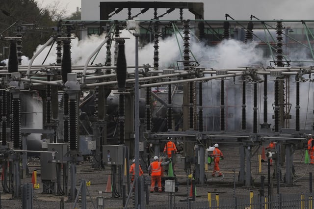 Workers are seen as smoke rises from the North Hyde electrical substation, which caught fire last night, leading to the closure of the Heathrow Airport, in London, Friday March 21, 2025.(AP Photo/Kirsty Wigglesworth)