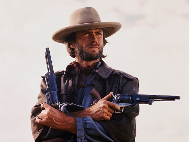 (Original Caption) Movie still of Clint Eastwood starring in the 1976 Western The Outlaw Josey Wales, directed by Clint Eastwood himself. Photo shows him from the waist-up holding two pistols, one pointing to his left and one pointing up, arms crossed.