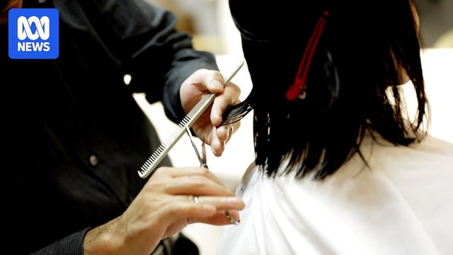 A close-up of hands holding scissors and a comb, cutting hair.