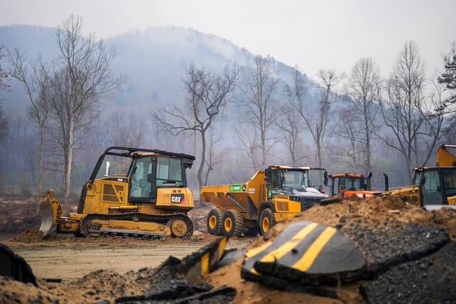 Smoke rises from a mountain ridge near storm debris and heavy machinery at the Black Cove wildfire on March 24, 2025, in Polk County near Saluda, North Carolina.