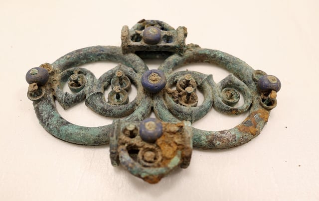 A copper alloy strap from a harness with blue glass decoration found in the hoard.