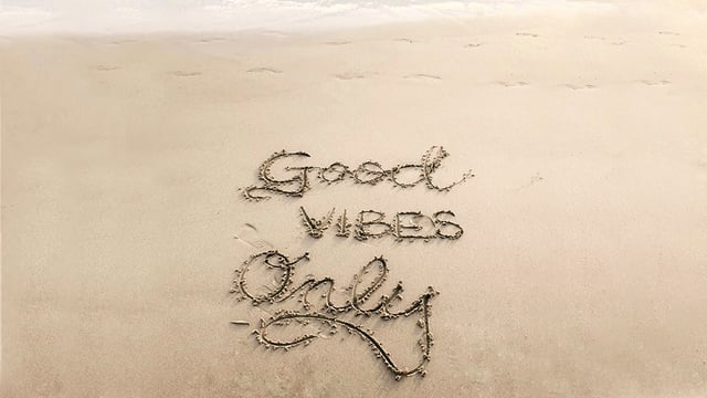 An image of a beach with text written in the sand reading 'Good vibes only'