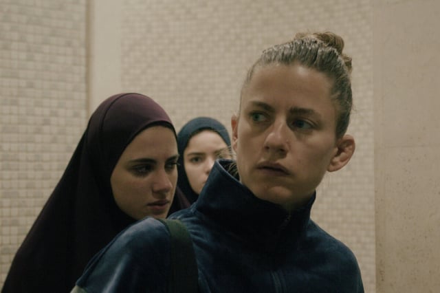 Sarah (Florentina Holzinger) mit zwei jungen Frauen mit Hidschab in einem anonymen Gebäude.