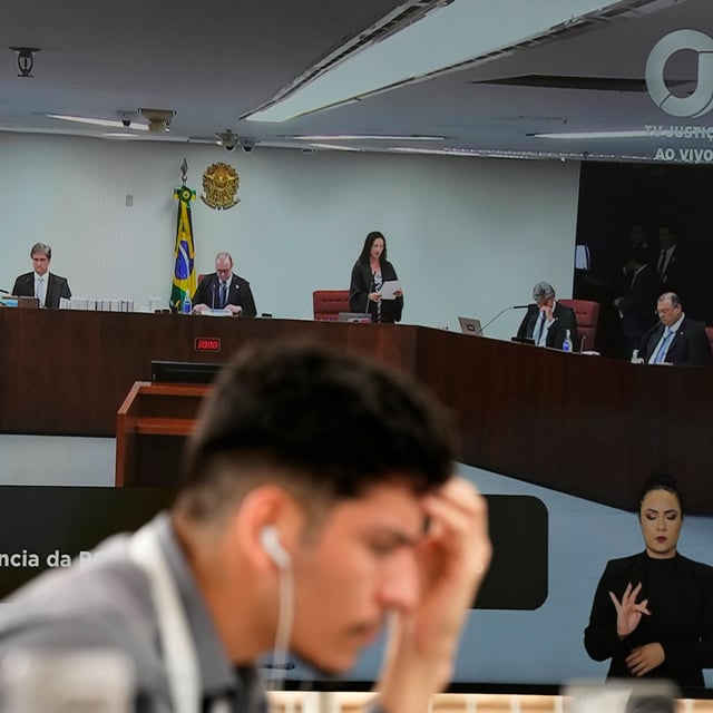 A journalist, foreground, attends the trial of Brazil's former President Jair Bolsonaro, on the large screen behind, in an external area of the Supreme Court in Brasilia, Brazil, Tuesday, March 25, 2025. (AP Photo/Eraldo Peres)
