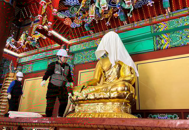 An official wraps a Buddha statue with a fire-retardant blanket to protect it from a wildfire, at Gounsa temple in Uiseong, South Korea, March 25, 2025.    REUTERS/Minwoo Park