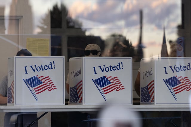 People complete their ballots as the sunset is reflected in the glass of a precinct in the Bloomfield neighborhood of Pittsburgh, Pennsylvania, on November 5, 2024.