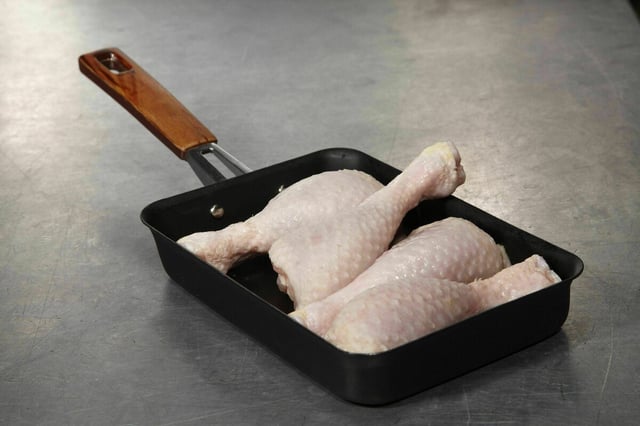 Vier rohe Hühnchenkeulen liegen in einer eckigen Bratpfanne