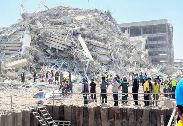 Des personnes se tiennent près d’un bâtiment effondré après qu’un fort tremblement de terre a frappé le centre du Myanmar vendredi 28 mars 2025