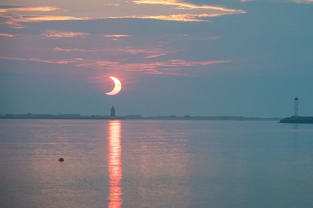 A partial solar eclipse is seen as the Sun rises behind the Delaware Breakwater Lighthouse on June 10, 2021, at Lewes Beach in Delaware.