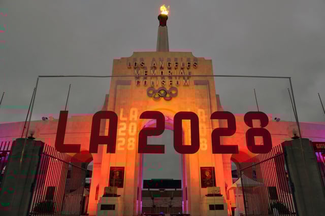 FILE – An LA 2028 sign is seen in front of the Olympic cauldron at the Los Angeles Memorial Coliseum, Wednesday, Sept. 13, 2017. The 2028 Los Angeles Olympics have announced more venue assignments, with the cities of Carson and Long Beach reprising their roles from previous games held in the region. (AP Photo/Richard Vogel, File)