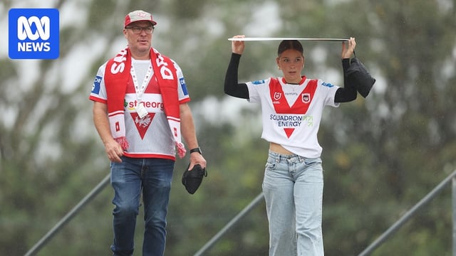 Father and daughter walk into stadium, wearing team gear, as rain falls