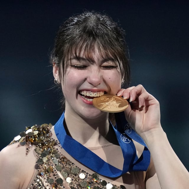 Gold medalist Alysa Liu, of the United States bites her medal during a ceremony for the women's free skating program at the figure skating world championships, Friday, March 28, 2025, in Boston. (AP Photo/Charles Krupa)