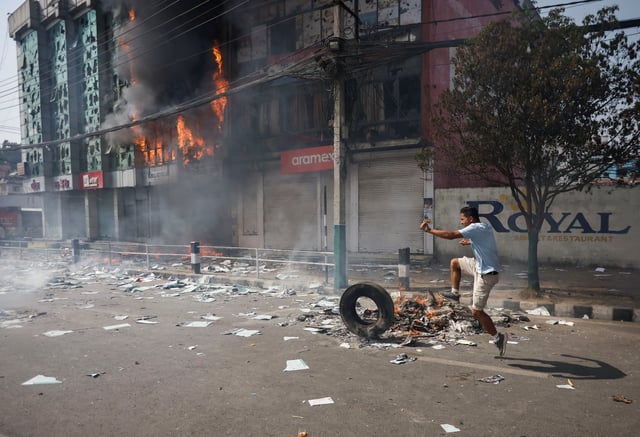 A pro-monarchist demonstrator kicks a tire next to a burning building during a protest demanding the restoration of Nepal's monarchy, which was abolished in 2008, saying the governments have failed to make any significant changes, in Kathmandu, Nepal, March 28, 2025. REUTERS/Navesh Chitrakar