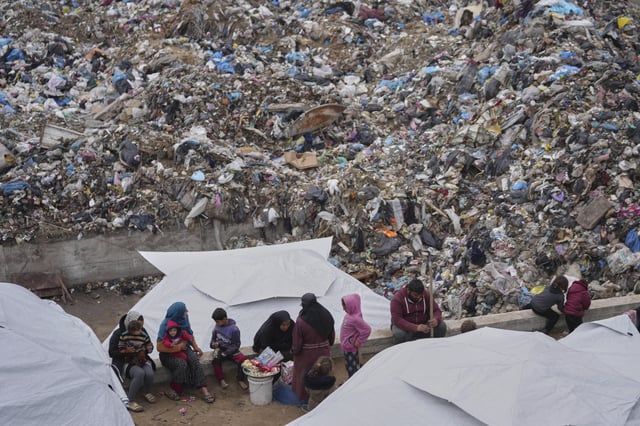 Palestinians displaced by the Israeli air and ground offensive on the Gaza Strip sit in a makeshift tent camp inside a landfill in central Gaza Strip, Friday, March 21, 2025. (AP Photo/Jehad Alshrafi)