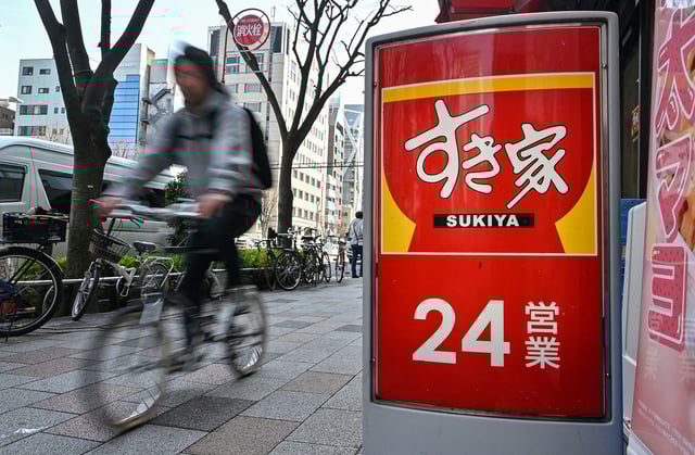A cyclist rides past a branch of Japanese fast-food restaurant chain Sukiya, famous for its beef bowls, along a street in downtown Tokyo on March 30, 2025.