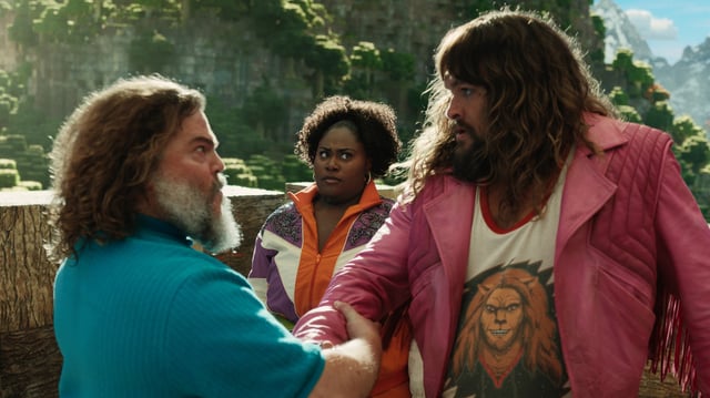 Jason Momoa and Jack Black shake a hand in minecraft while a captive audience of one watches.