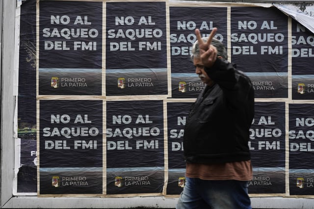 A pedestrian flashes a victory sign as he passes posters that read in Spanish "No to IMF plundering" in Buenos Aires, Argentina, Monday, March 31, 2025. (AP Photo/Natacha Pisarenko)