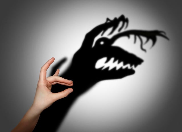 A hand projects a scary shadow on the wall behind.