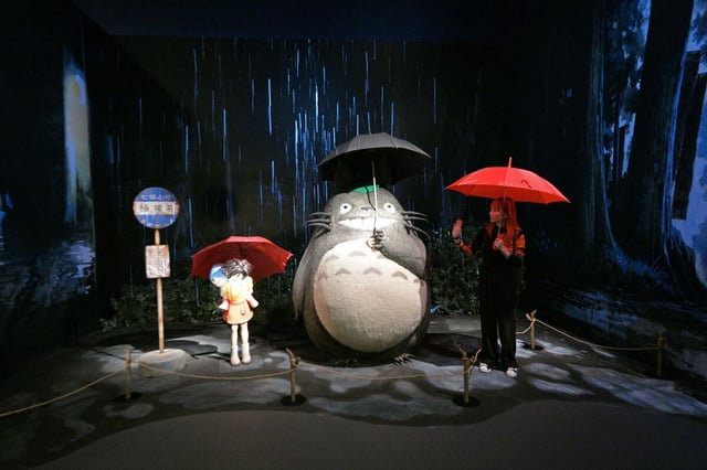 Ausstellung über "Die Welt der Ghibli Studios": eine Person mit Regenschirm posiert für ein Selfie neben den Skulpturennachbildungen der berühmten Regenschirmszene aus "Mein Nachbar Totoro"