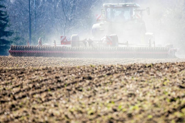 Ein Traktor zieht eine Egge über einen Acker und zieht eine Staubwolke hinter sich her