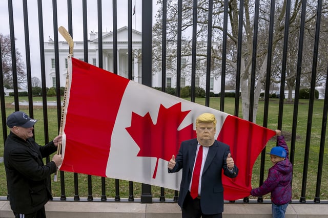 Toronto residents Douglas Bloomfield, left, and his son Phoenix, right, who are on vacation in Washington, hold a Canadian flag and an ice hockey stick to show their support for Canada regarding trade tariffs as they pose with with another visitor to the city wearing a mask of President Donald Trump in front of the White House in Washington, Thursday, March 13, 2025. (AP Photo/Ben Curtis)