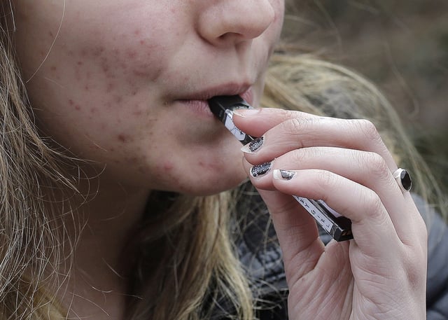 FILE - A high school student uses a vaping device near a school campus in Cambridge, Mass., April 11, 2018. (AP Photo/Steven Senne, File)