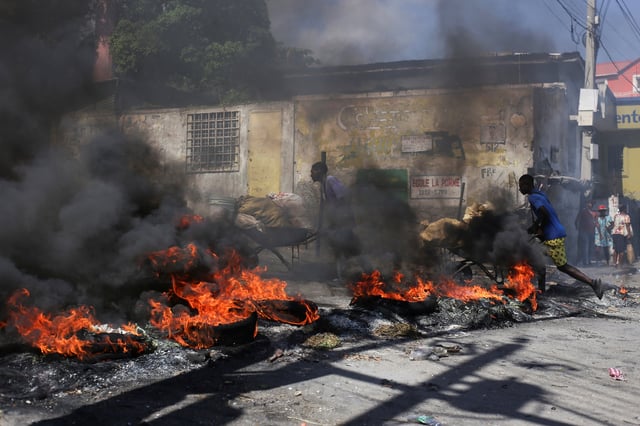 People push wheelbarrows past a burning barricade during a protest against insecurity, in Port-au-Prince, Haiti April 2, 2025. REUTERS/Jean Feguens Regala