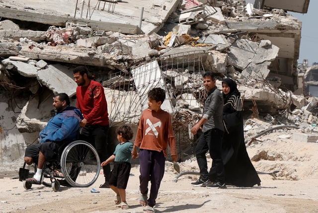 Palestinians walk by the rubble of houses, in Khan Younis in the southern Gaza Strip, April 3, 2025. REUTERS/Hatem Khaled