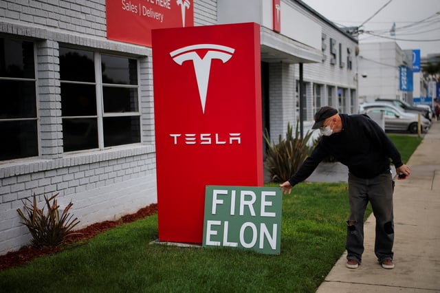 A man places a sign outside a Tesla dealership during a protest against Tesla and its CEO Elon Musk outside a Tesla dealership in Los Angeles, California, U.S. March 14, 2025. REUTERS/Daniel Cole/File Photo