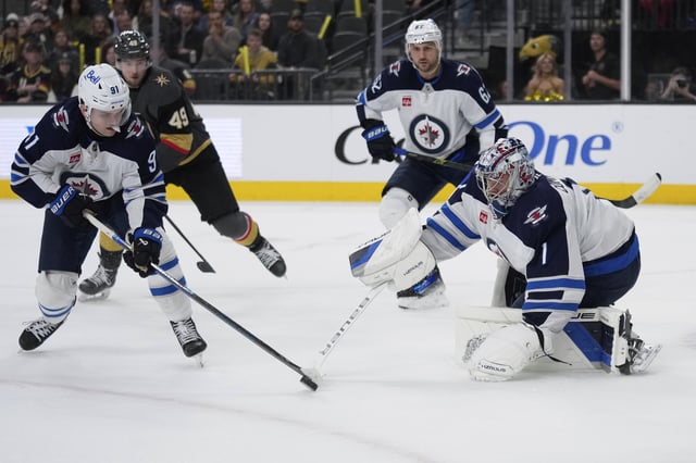 Winnipeg Jets goaltender Eric Comrie (1) knocks the puck to Winnipeg Jets center Cole Perfetti (91) during the second period of an NHL hockey game against the Vegas Golden Knights, Thursday, April 3, 2025, in Las Vegas. (AP Photo/John Locher)