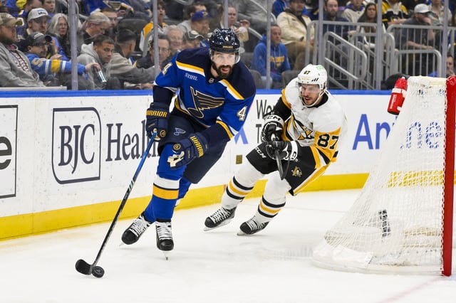 Apr 3, 2025; St. Louis, Missouri, USA;  St. Louis Blues defenseman Nick Leddy (4) controls the puck as Pittsburgh Penguins center Sidney Crosby (87) defends during the third period at Enterprise Center. Mandatory Credit: Jeff Curry-Imagn Images