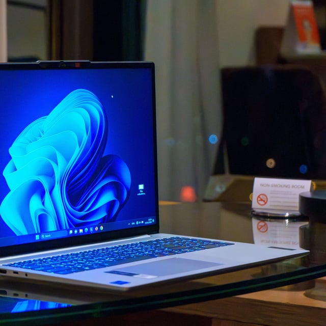 A laptop with the Windows 11 desktop on screen, glowing, while on a work desk 