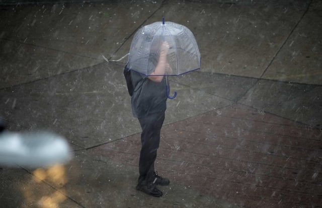 A pedestrian seeks shelter under an umbrella as heavy rain packing high winds and large hail sweeps over downtown Denver on Thursday, June 29, 2023.