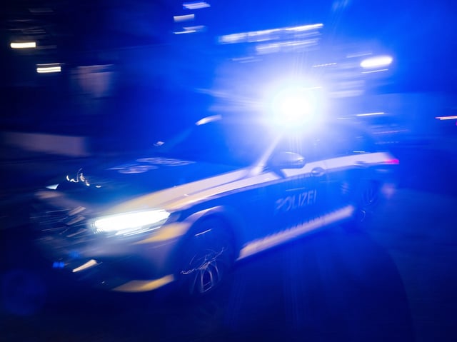 Ein Polizeifahrzeug fährt mit Blaulicht an einem Gebäude vorbei (Symbolbild)
