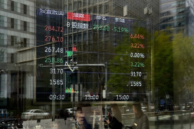 Pedestrian are reflected on a brokerage house&#39;s window as an electronic board displays shares trading index, in Beijing, Monday, April 7, 2025.