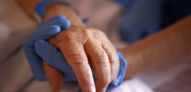 Un personnel soignant tient la main d'un patient en soins palliatifs, à l'hôpital Eugénie d'Ajaccio, le 23 avril 2020