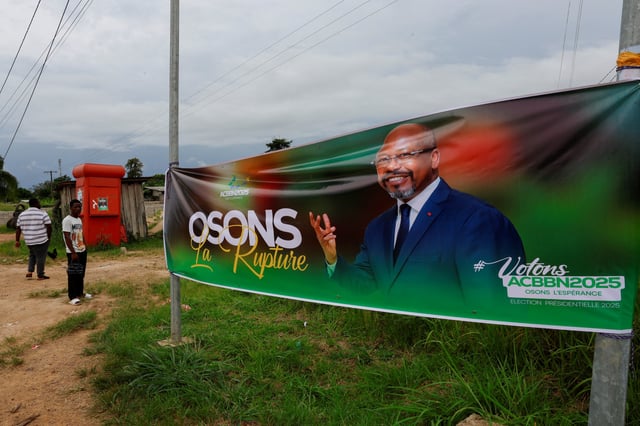 People stand near an electoral banner of Alain Claude Bilie By Nze, former Prime Minister and presidential candidate, ahead of the 2025 Gabonese presidential election in Lambarene, Gabon April 8, 2025. REUTERS/Luc Gnago