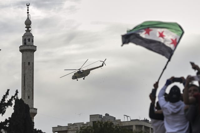 Confetti and flowers are dropped from a military helicopter onto a crowd during a celebration marking the 10th anniversary of the victory of rebel forces over Bashar al-Assad's army in Idlib, Syria, Friday, March 28, 2025. (AP Photo/Ghaith Alsayed)