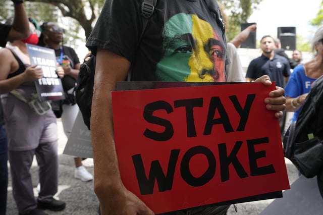 A person carries a Stay Woke sign during a march to the School Board of Miami-Dade County to protest Florida&#39;s new teaching standards on August 16, 2023, in Miami.