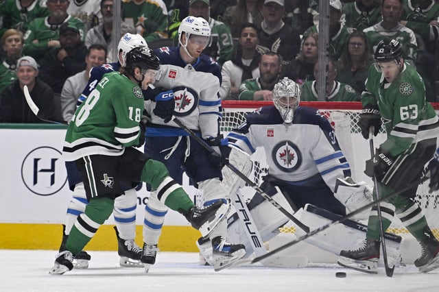 Apr 10, 2025; Dallas, Texas, USA; Dallas Stars center Sam Steel (18) and right wing Evgenii Dadonov (63) try to redirect the puck past Winnipeg Jets goaltender Connor Hellebuyck (37) during the first period at the American Airlines Center. Mandatory Credit: Jerome Miron-Imagn Images