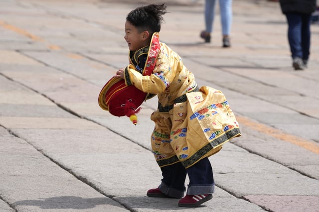 A child dressed as the emperor reacts after retrieving his crown blown away outside the Forbidden City during high winds in Beijing, China, Saturday, April 12, 2025. (AP Photo/Ng Han Guan)