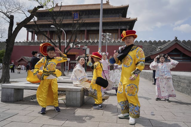 Tourists dressed as emperors react to strong winds outside the Forbidden City in Beijing, China, Saturday, April 12, 2025. (AP Photo/Ng Han Guan)