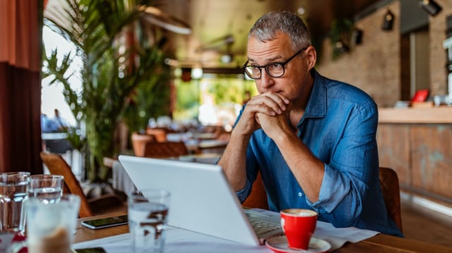 Mature man using laptop in a cafe, looking annoyed