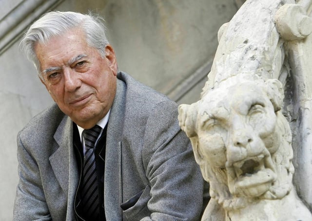 Ein grauhaariger Mann sitzt neben einer Steinbüste