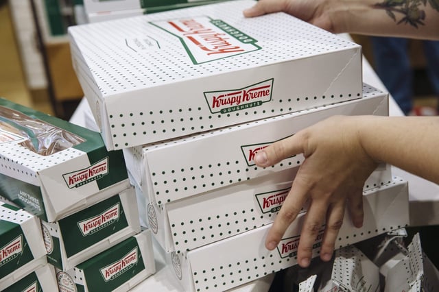 An employee carries boxes of doughnuts inside a Krispy Kreme store.