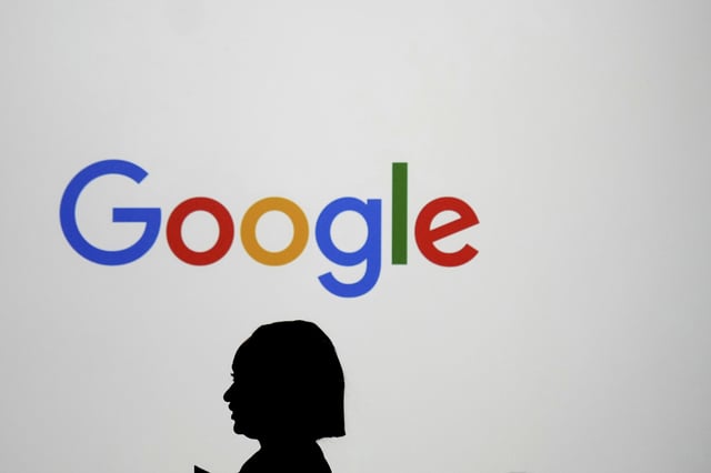 FILE - A woman walks by a giant screen with a logo at an event at the Paris Google Lab on the sidelines of the AI Action Summit in Paris, Sunday, Feb. 9, 2025. (AP Photo/Thibault Camus, File)