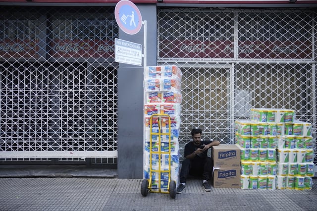 A worker sits outside a supermarket waiting for the store to open to deliver toilet paper in Buenos Aires, Argentina, Monday, April 14, 2025. (AP Photo/Natacha Pisarenko)